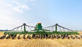 Agricultural seeder against the background of a wide field on yellow stubble and a blue cloudy sky on a summer day Royalty Free Stock Photo