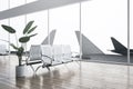 Modern airport waiting area interior with reflections on floor, wooden flooring, decorative plants, benches, window with aircraft