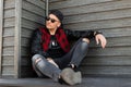 Modern American handsome young hipster man in stylish clothes in a stylish black baseball cap in trendy sunglasses sits Royalty Free Stock Photo