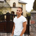 Modern American man with a fashionable hairstyle in a stylish white T-shirt stands near the wrought vintage gates near the house.