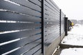 Modern anthracite panel fencing, with a visible fence foundation connector, it rains in winter, in the background there is snow Royalty Free Stock Photo