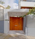 A modern apartment building main entrance, natural wooden door by the sidewalk.