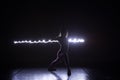 Modern art dancer, dancing in front of a black background with neon blue light while stretching and twisting her body