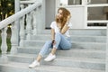 Modern attractive stylish young woman in a fashionable t-shirt in blue jeans in white sneakers resting sitting Royalty Free Stock Photo