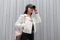 Modern attractive young woman in a stylish baseball cap in a vintage white leather jacket in black jeans Royalty Free Stock Photo