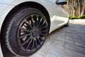 Modern auto wheel of car with beautiful black alloy disc and fresh rubber tread on paving slab with green pines on sunset