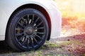 Modern auto wheel of car with beautiful black alloy disc and fresh rubber tread on rustic forest road with green grass on sunset