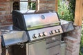 Modern barbecue grill from stainless steel in a shelter made of old bricks in the backyard garden, outdoor cooking concept,