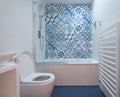 Modern bathroom with bath, toilet, niche in wall and basin unit, blue rubber floor and blue and white patchwork tiles