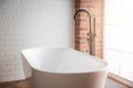 Modern bathroom with freestanding white bathtub and black faucet. Brick walls in loft style