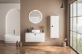 Modern bathroom interior with beige walls, white basin with oval mirror, bathtub and parquet floor. Minimalist beige bathroom with Royalty Free Stock Photo