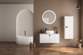 Modern bathroom interior with beige walls, white basin with oval mirror, bathtub and parquet floor. Minimalist beige bathroom with Royalty Free Stock Photo