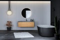 Modern bathroom interior with concrete floor, black bathtub, and oval mirror, marble basin, pendant light, cactus, front view. Royalty Free Stock Photo