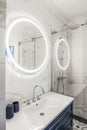 Modern bathroom interior with a dark blue wooden shelf, white sink and big round mirror with LED light. Royalty Free Stock Photo