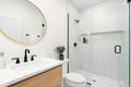 A modern bathroom with a wood cabinet, gold mirror, and marble tiled shower. Royalty Free Stock Photo