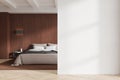 Modern bedroom with bed, pillows, and side table. Empty wall space on right for mockup. Wooden floor and paneling. Royalty Free Stock Photo