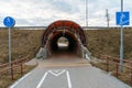 A modern bike path with markings and road signs. The bicycle road runs through a tunnel through a busy highway. A recreation area