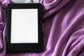 A modern black e-reader electronic book with a blank screen on a gray and purple bed. Mockup template tablet on microfiber bedding