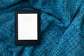 A modern black electronic book with a blank screen on a bright blue knitted blanket. Mockup tablet