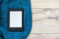 A modern black electronic book with a blank screen on a bright blue knitted blanket on a wooden floor. Mockup tablet
