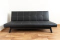 Modern black leather convertible sofa bed, wooden floor. Empty waiting room with a modern black sofa