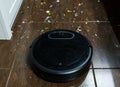 Modern black robotic vacuum cleaner removing litter from brown wooden floor. Cleaning at home, top view.