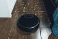 Modern black robotic vacuum cleaner removing litter from brown wooden floor. Cleaning at home, top view