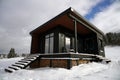 Modern black tiny cabin in snowy weather with stacked firewood under Royalty Free Stock Photo