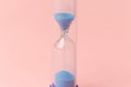 Modern blue Hourglass on pink background. Sand trickling through the bulbs of a crystal sand glass. Symbol of time Royalty Free Stock Photo
