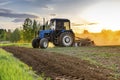 Modern blue tractor machinery plowing agricultural field meadow at farm at spring autumn during sunset.Farmer cultivating,make Royalty Free Stock Photo