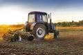 Modern blue tractor machinery plowing agricultural field meadow at farm at spring autumn during sunset.Farmer