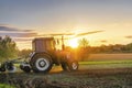 Modern blue tractor machinery plowing agricultural field meadow at farm at spring autumn during sunset.Farmer