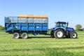 Modern blue tractor pulling a trailer in grass field