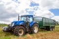 Modern blue tractor pulling a trailer in harvest field Royalty Free Stock Photo