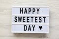 Modern board with text `Happy Sweetest Day` word over white wooden surface, top view. From above, flat lay