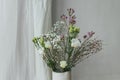 Modern bouquet in vase against tulle and rustic wall. Stylish spring flowers, eustoma, gypsophila and chamelaucium