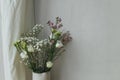 Modern bouquet in vase against tulle and rustic wall. Stylish spring flowers, eustoma, gypsophila and chamelaucium