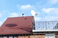 Modern brick private house with red shingle tile rooftop, satellite dish antennas, open balcony on bright blue sky, bottom view.