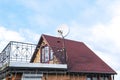 Modern brick private house with red shingle tile rooftop, satellite dish antennas, open balcony on bright blue sky, bottom view.