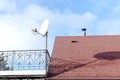 Modern brick private house with red shingle tile rooftop, satellite dish antennas, open balcony on bright blue sky, bottom view.