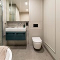 Modern bright bathroom with beige wall. Washbasin with turquoise cupboard and mirror. Wall with molding