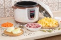 Modern, light multi cooker and raw products on table in kitchen. Cooking stewed potatoes with meat in multicooker Royalty Free Stock Photo