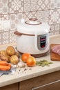 Modern, light multi cooker and raw products on table in kitchen. Cooking stewed potatoes with meat in multicooker Royalty Free Stock Photo