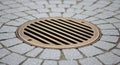 Modern Bronze Circular Drain Grate Embedded in Textured Grey Cobblestone Pavement with Shallow Depth of Field Royalty Free Stock Photo