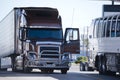 Modern brown big rig semi truck with open door and reefer trailer on truck stop Royalty Free Stock Photo