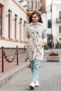 Modern brown-haired young woman in fashionable spring clothes in white stylish sneakers travels along the street near vintage Royalty Free Stock Photo