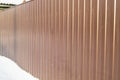 Modern brown metal corrugated siding fence, outdoor winter space, safety and security, veneer texture Royalty Free Stock Photo