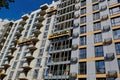 Modern building under construction against blue sky. Professional builders working in cradles on the facade of a