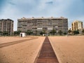 Modern buildings next to the beach with a wooden walkway leading to them on a cloudy and rainy day i