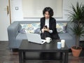 Modern business caucasian woman checking something on her phone, sitting on the sofa with her laptop and a cup of coffee Royalty Free Stock Photo